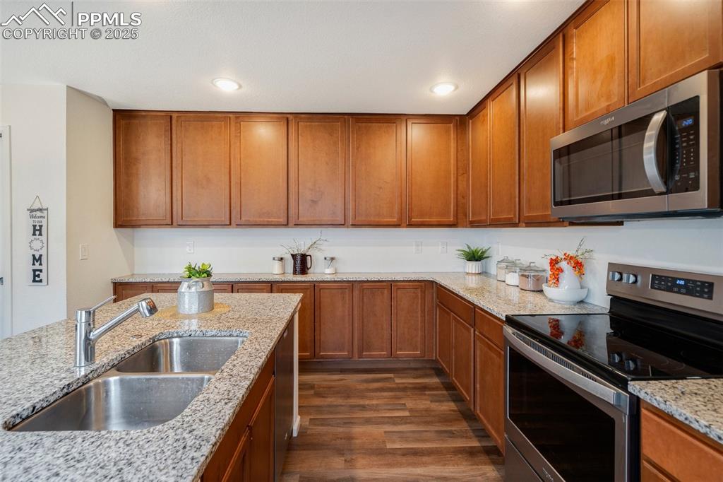 Image 12 of 29: Kitchen with brown cabinetry, stainless steel appliances, dark wood-type fl