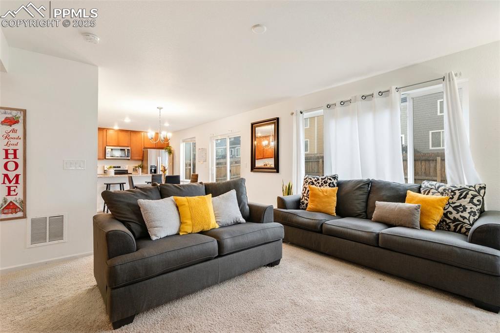 Image 4 of 29: Living area with light carpet, visible vents, and an inviting chandelier