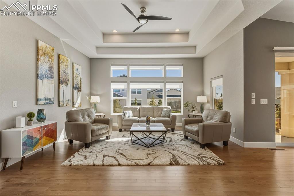 Image 17 of 49: Living room featuring dark wood-style floors, a ceiling fan, a tray ceiling