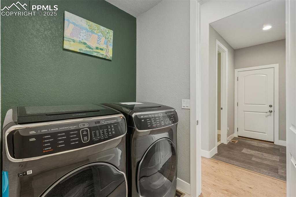 Image 26 of 49: Laundry room with a textured wall, light wood finished floors, and washer a