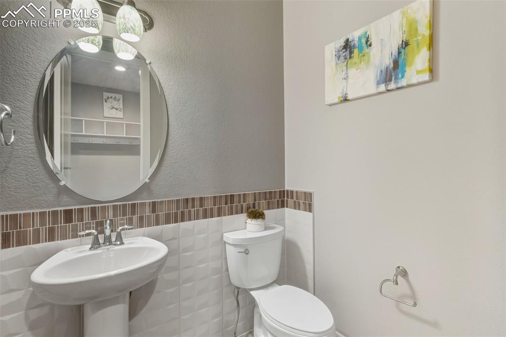 Image 28 of 49: Bathroom with tile walls, a textured wall, and a wainscoted wall