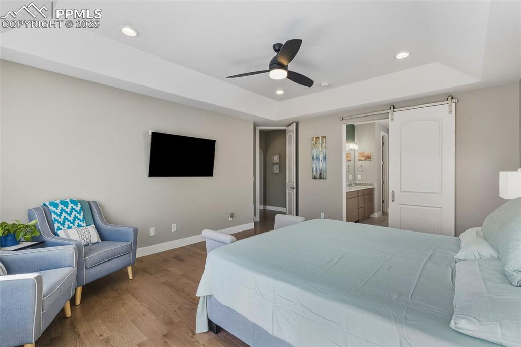 Image 35 of 49: Bedroom featuring a barn door, wood finished floors, a raised ceiling, rece