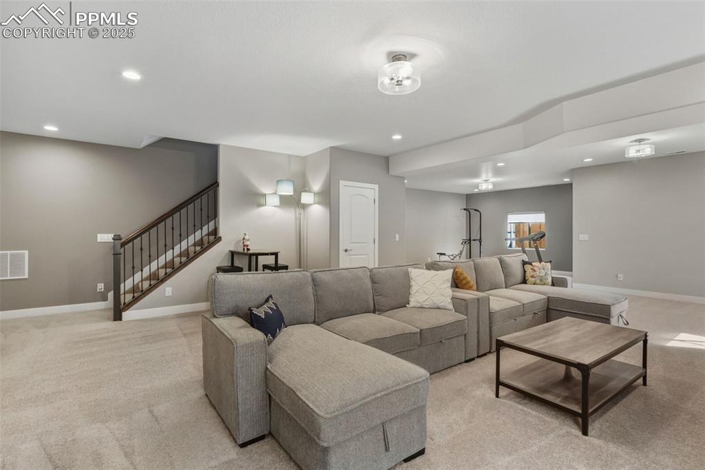 Image 37 of 49: Living area with recessed lighting, light carpet, and stairs
