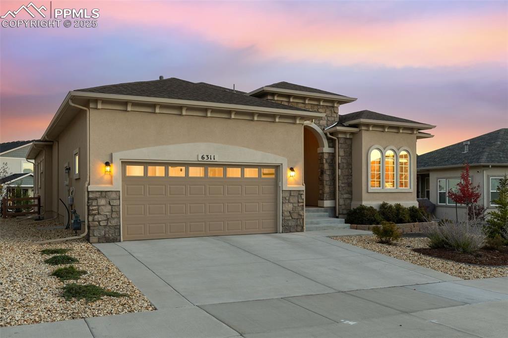 Image 8 of 49: View of front of home with stone siding, an attached garage, and stucco sid