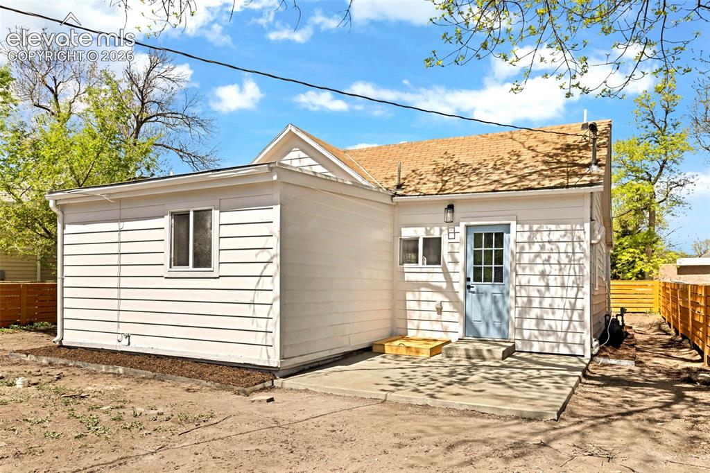 Image 6 of 26: White horizontal siding exterior with a light blue entry door, concrete pat