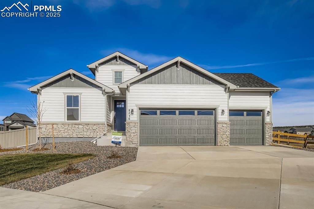 Caption: View of front facade featuring stone siding, driveway, a garage, and board and batten siding