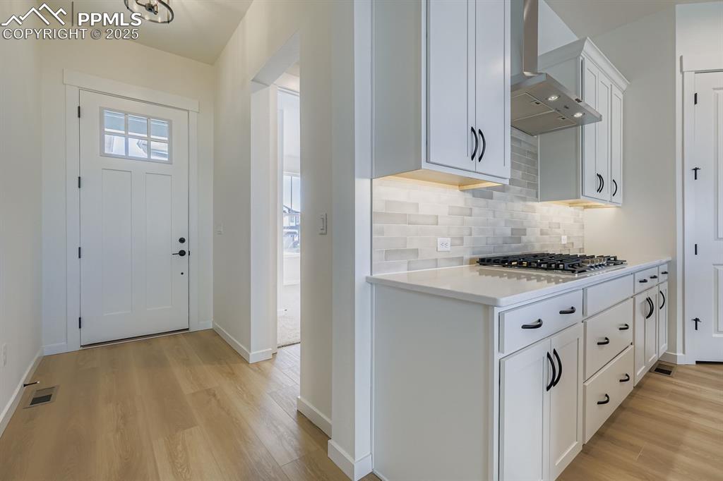 Image 4 of 27: Kitchen with white cabinetry, light wood-type flooring, wall chimney exhaus