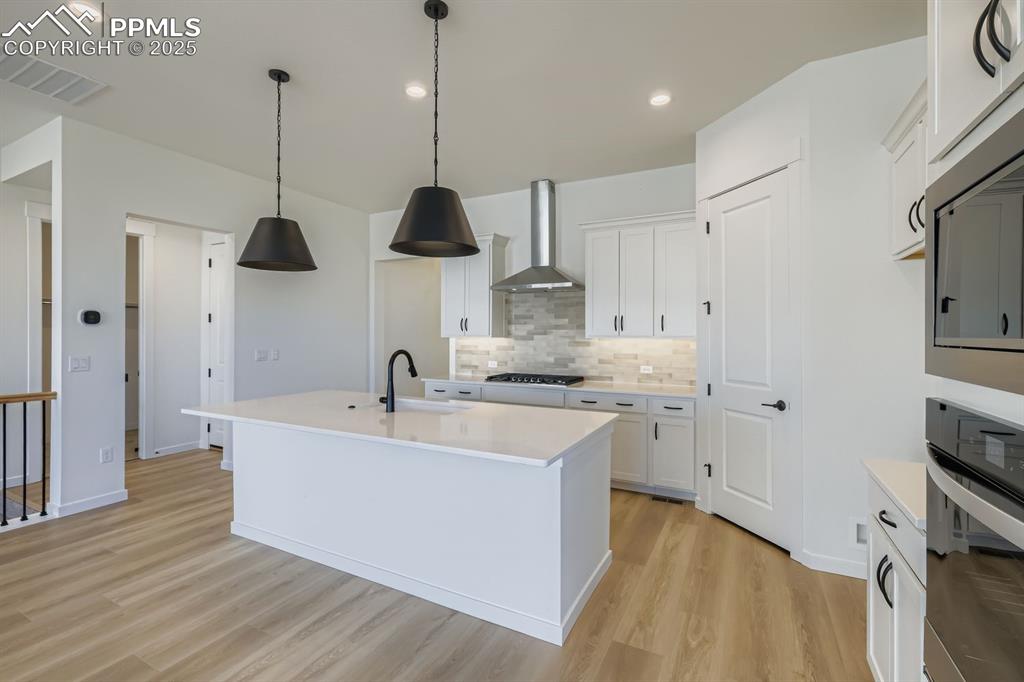 Image 9 of 27: Kitchen featuring a kitchen island with sink, decorative backsplash, stainl
