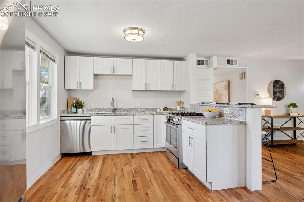 Image 13 of 20: Kitchen with white cabinetry, a peninsula, stainless steel appliances, and