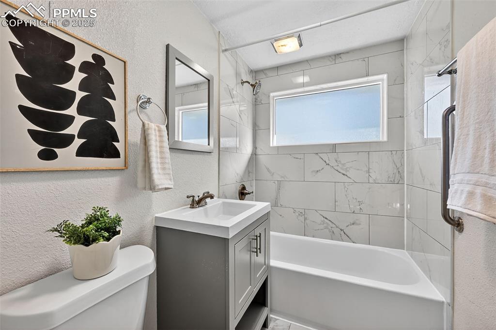 Image 15 of 20: Full bath featuring a textured wall, shower combination, and vanity