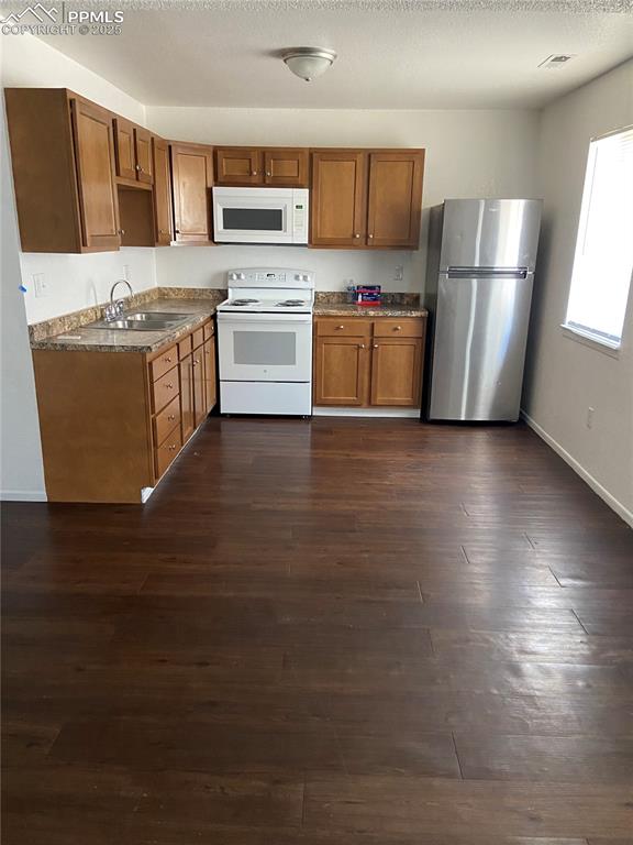 Image 6 of 8: Kitchen with oak cabinetry, white appliances, a sink, and dark wood finishe