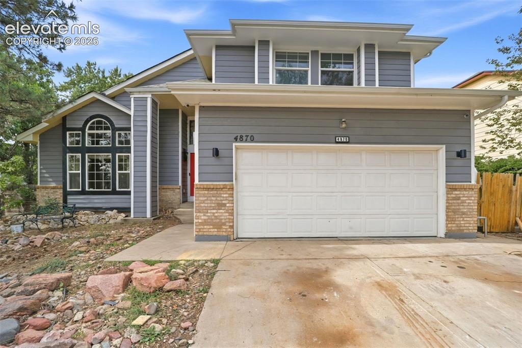 Caption: Contemporary exterior with gray siding, brick accents, arched window, and an integrated two-car gara