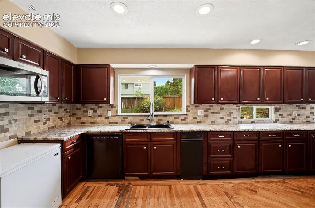 Image 12 of 34: Kitchen featuring wood-finish flooring, dark wood cabinetry, light-toned co