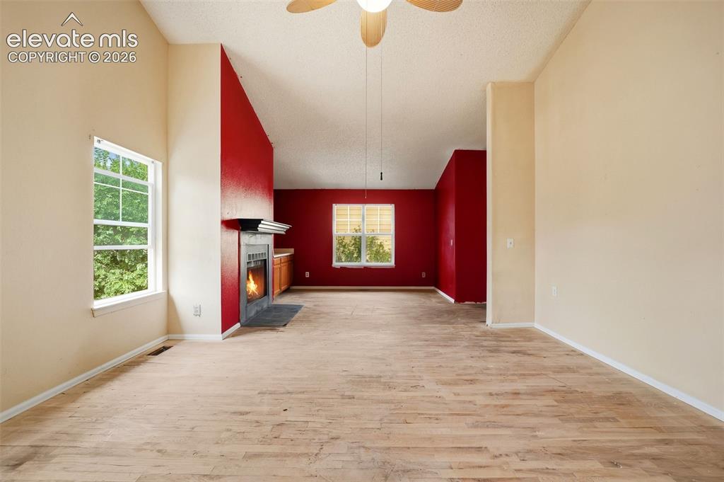 Image 23 of 34: Vaulted ceiling, ceiling fan, wood-finish flooring, fireplace with dark sto