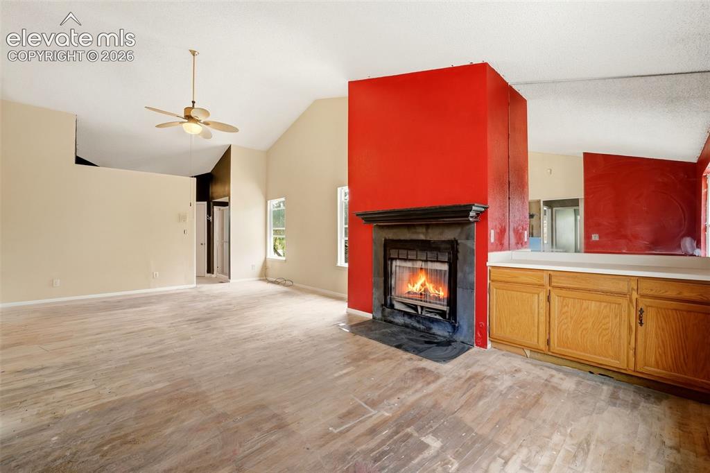Image 25 of 34: Vaulted ceiling with a ceiling fan, fireplace featuring a dark stone surrou