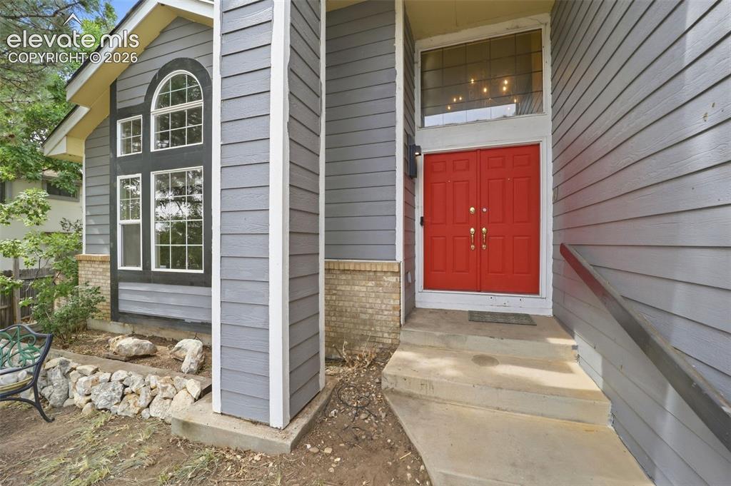 Image 3 of 34: Gray siding exterior with brick accents, red double entry doors, transom wi