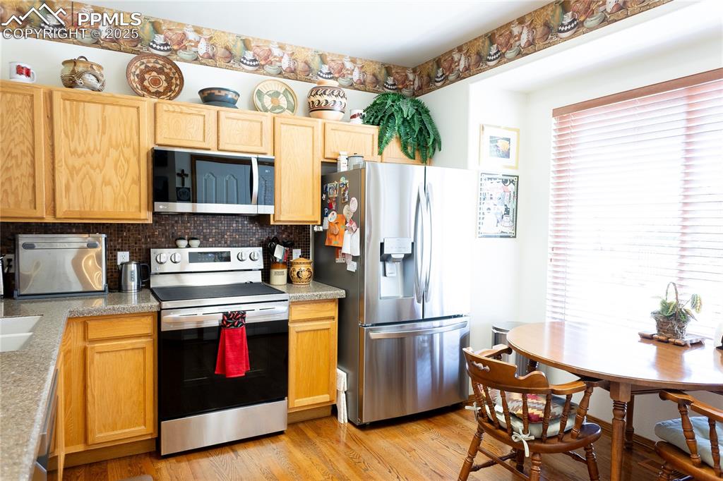 Image 13 of 48: Kitchen with appliances with stainless steel finishes, backsplash, light br