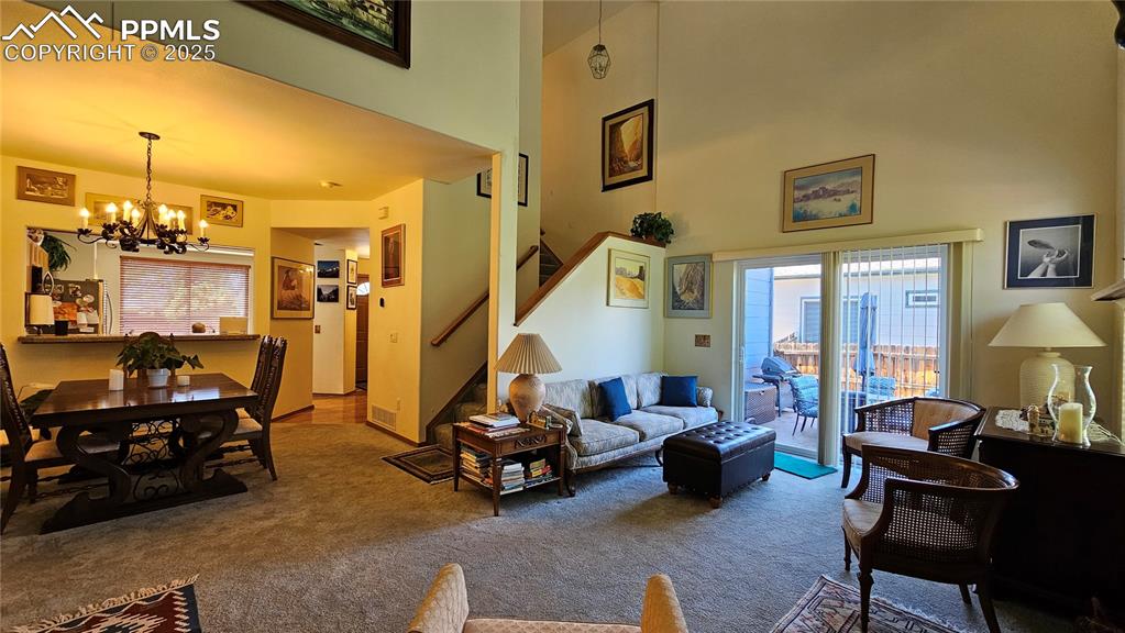 Image 18 of 48: Carpeted living room featuring stairs, a chandelier, and a high ceiling