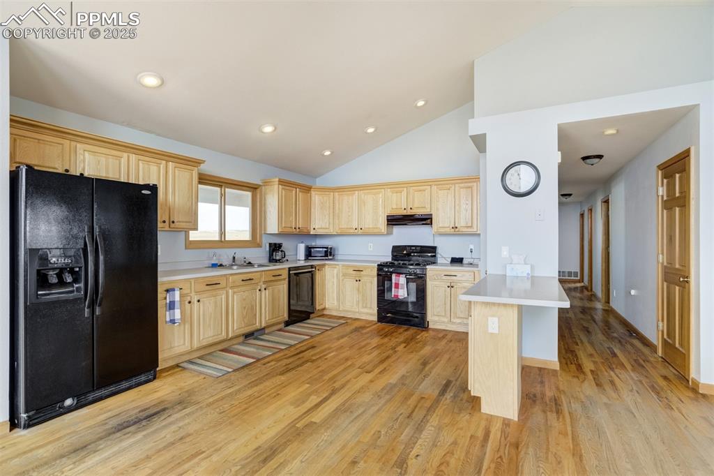 Image 15 of 50: Kitchen with light brown cabinetry, black appliances, a peninsula, light wo
