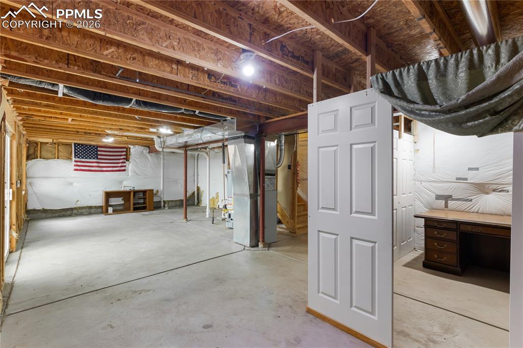 Image 40 of 43: Unfinished basement with exposed ceiling joists and concrete flooring, offe