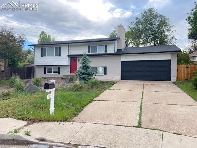 Caption: Split foyer home featuring a garage, concrete driveway, and a chimney