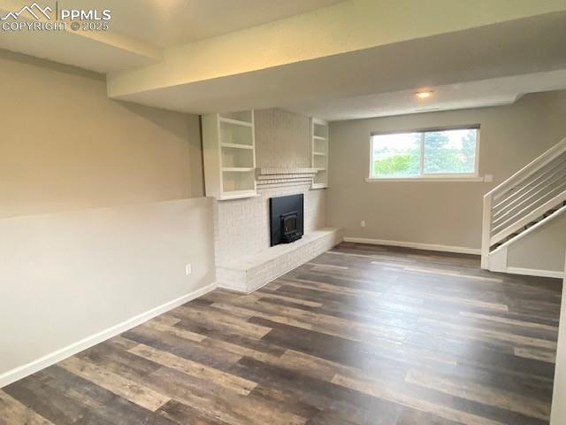 Image 16 of 26: Unfurnished living room with baseboards, dark wood-style flooring, and stai