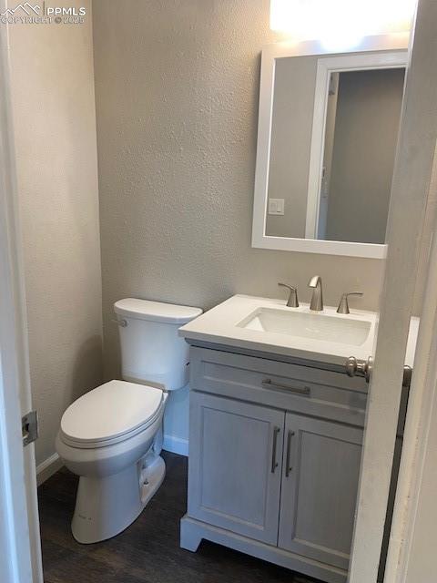 Image 7 of 26: Half bathroom with vanity, toilet, wood finished floors, a textured wall, a
