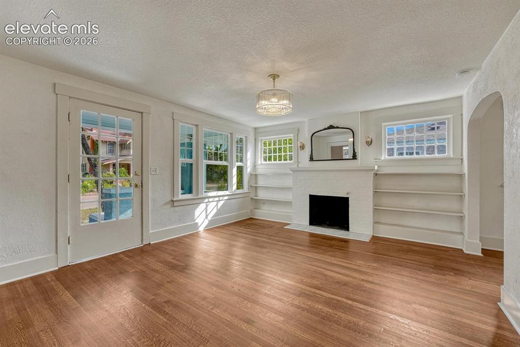 Image 11 of 44: Hardwood flooring, white brick fireplace, built-in shelving, glass-paned do