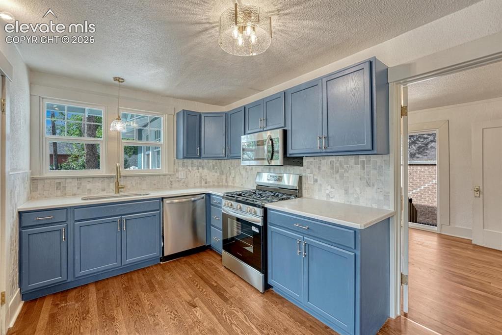 Image 14 of 44: Kitchen featuring blue cabinetry, light countertops, a tile backsplash, sta