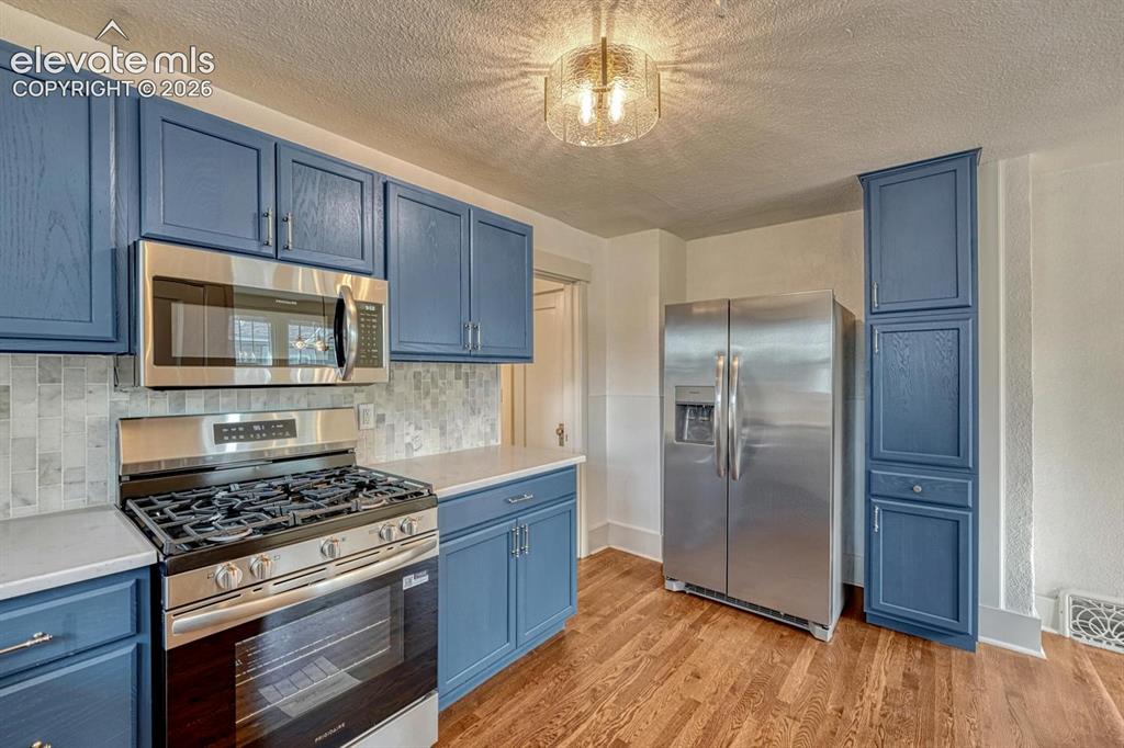 Image 17 of 44: Blue cabinetry with stainless steel appliances, mosaic tile backsplash, lig
