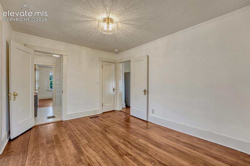 Image 21 of 44: Hardwood flooring, crown molding, white trim, recessed door frame, and a co