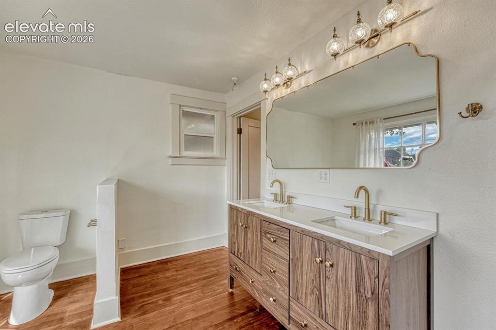 Image 23 of 44: Dual vanity with wood-finish cabinetry, white countertop, and gold-toned fi