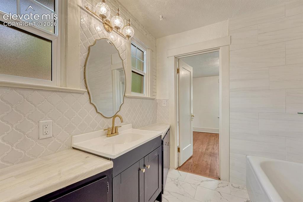 Image 25 of 44: White tile wainscoting and flooring, dark wood-finish vanity with a white c