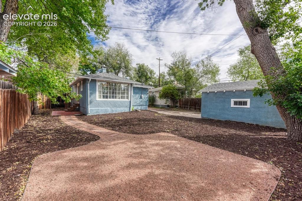 Image 33 of 44: Private backyard with a detached garage, mature trees, and a curved paved p