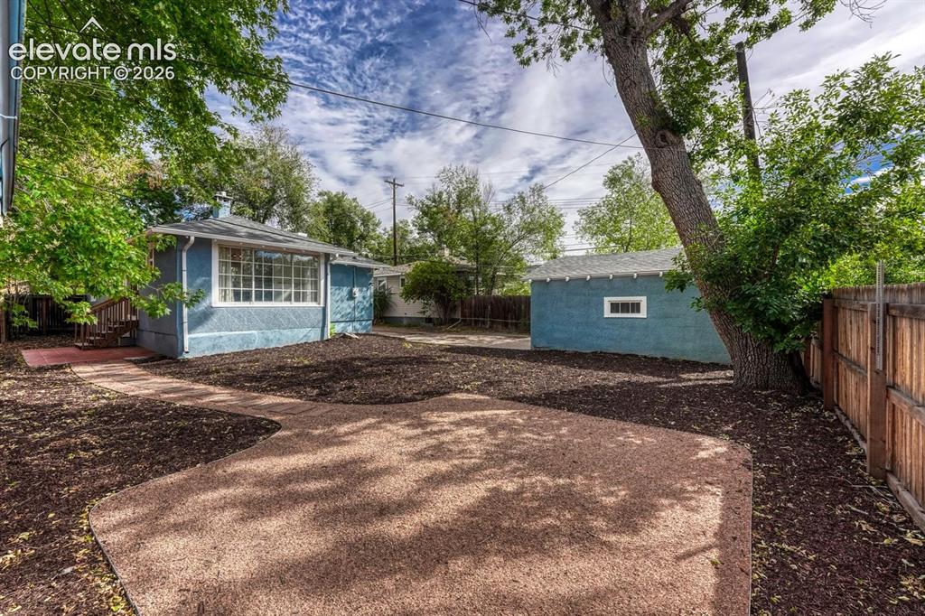 Image 41 of 44: Expansive backyard with a large patio area, mature trees, wood fencing, and