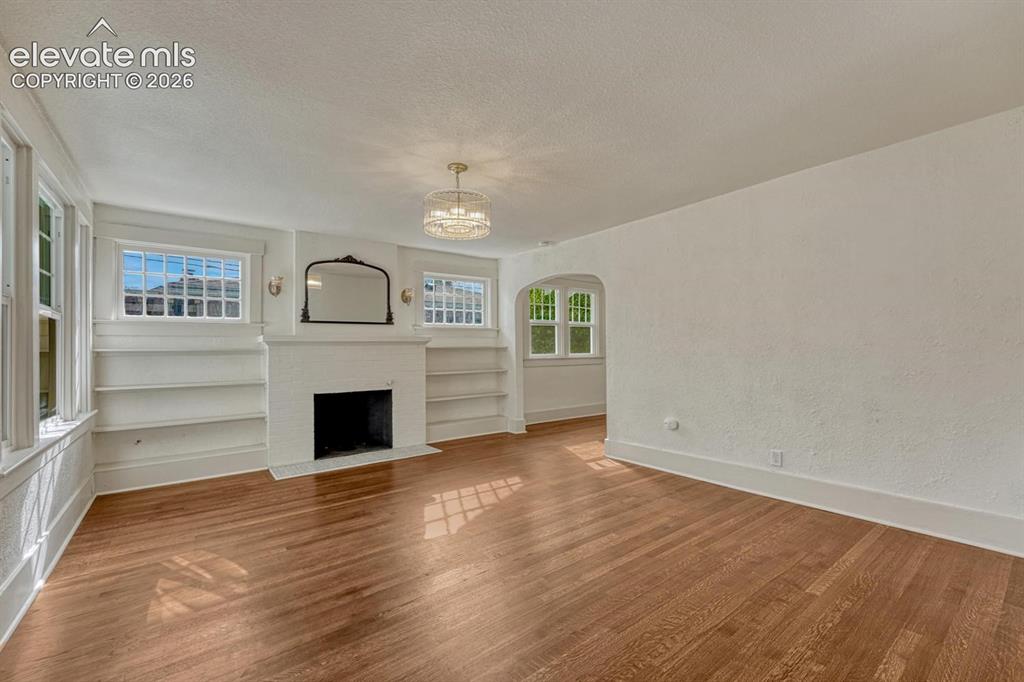 Image 8 of 44: Wood-finish flooring, built-in shelving, white fireplace, chandelier, and a