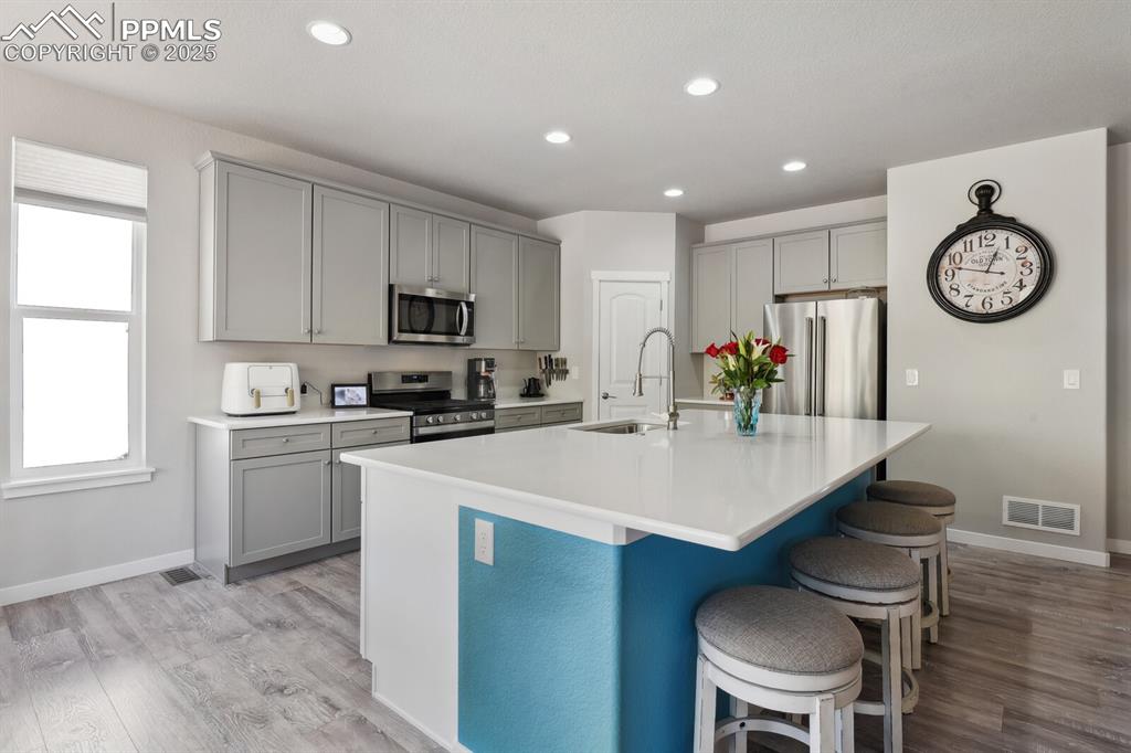 Image 15 of 47: Kitchen featuring stainless steel appliances, gray cabinetry, a breakfast b