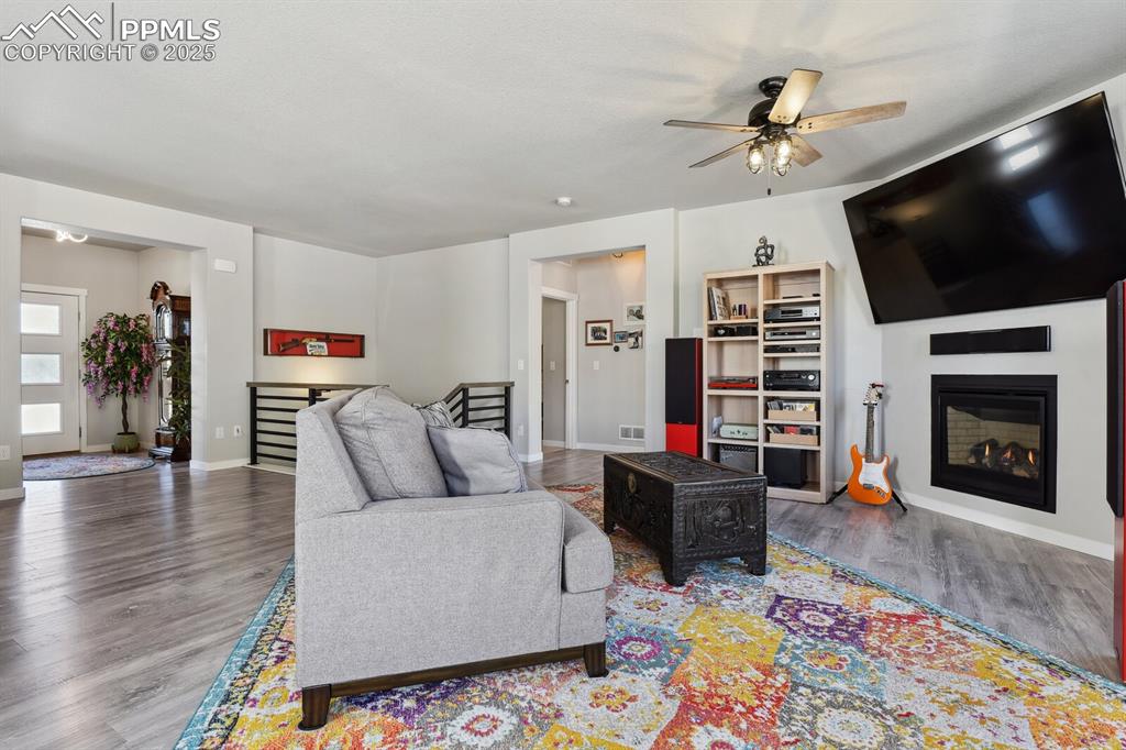 Image 19 of 47: Living room featuring wood finished floors, ceiling fan, and a glass covere