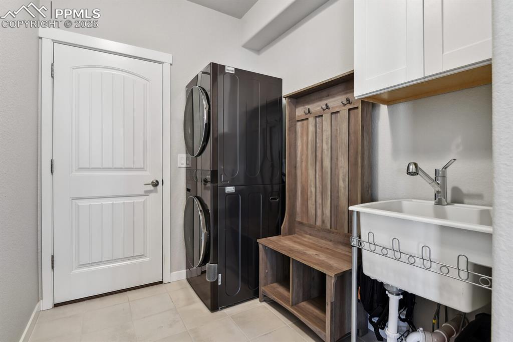 Image 24 of 47: Laundry area with cabinet space, stacked washer / dryer, and light tile pat