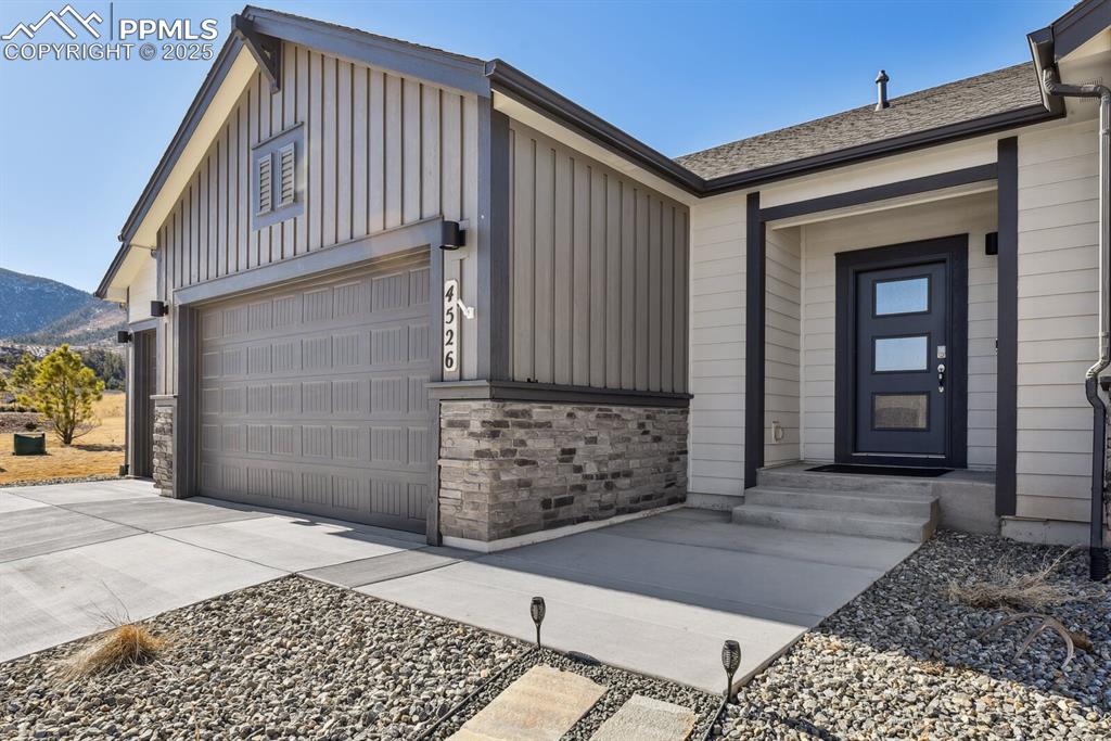 Image 4 of 47: View of exterior entry with board and batten siding, driveway, stone siding