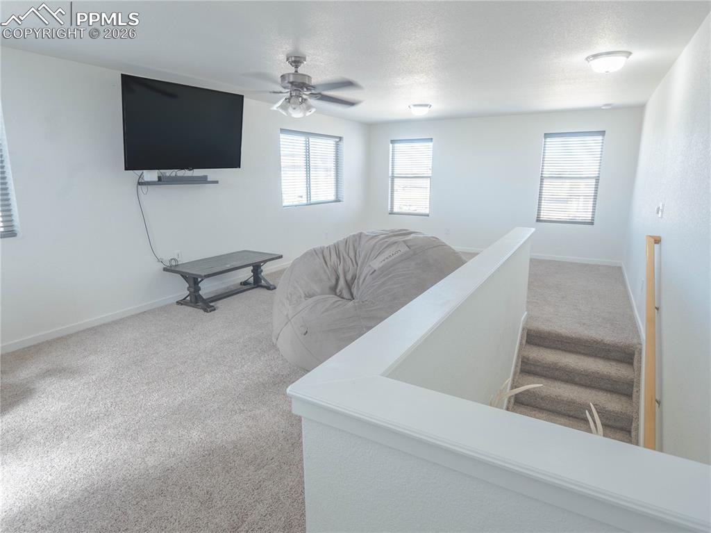 Image 22 of 30: Carpeted loft area with multiple windows and a ceiling fan