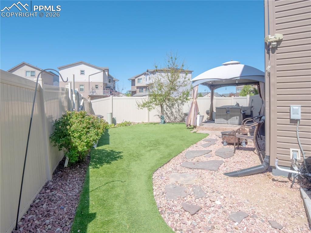 Image 25 of 30: Fenced backyard featuring artificial turf, a stone paver pathway, and a gra