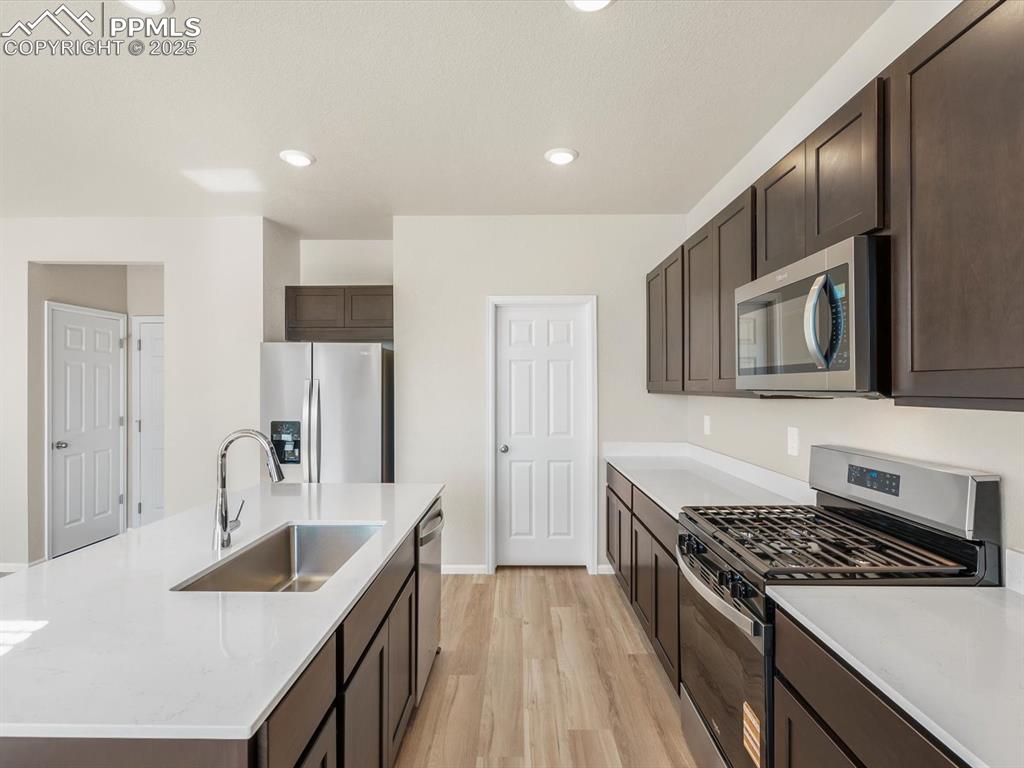Image 10 of 27: Kitchen with dark brown cabinets, stainless steel appliances, light wood-ty
