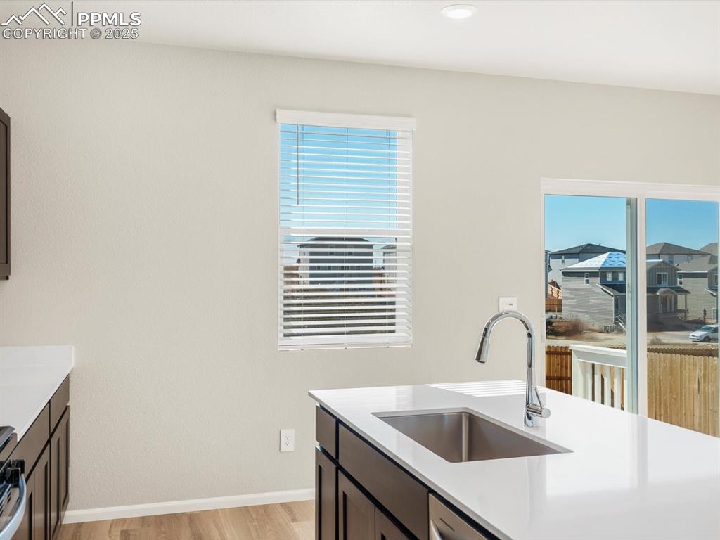Image 11 of 27: Kitchen with light wood-style flooring, light stone countertops, dark brown