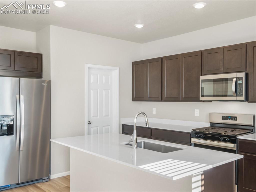 Image 9 of 27: Kitchen featuring stainless steel appliances, dark brown cabinets, light wo