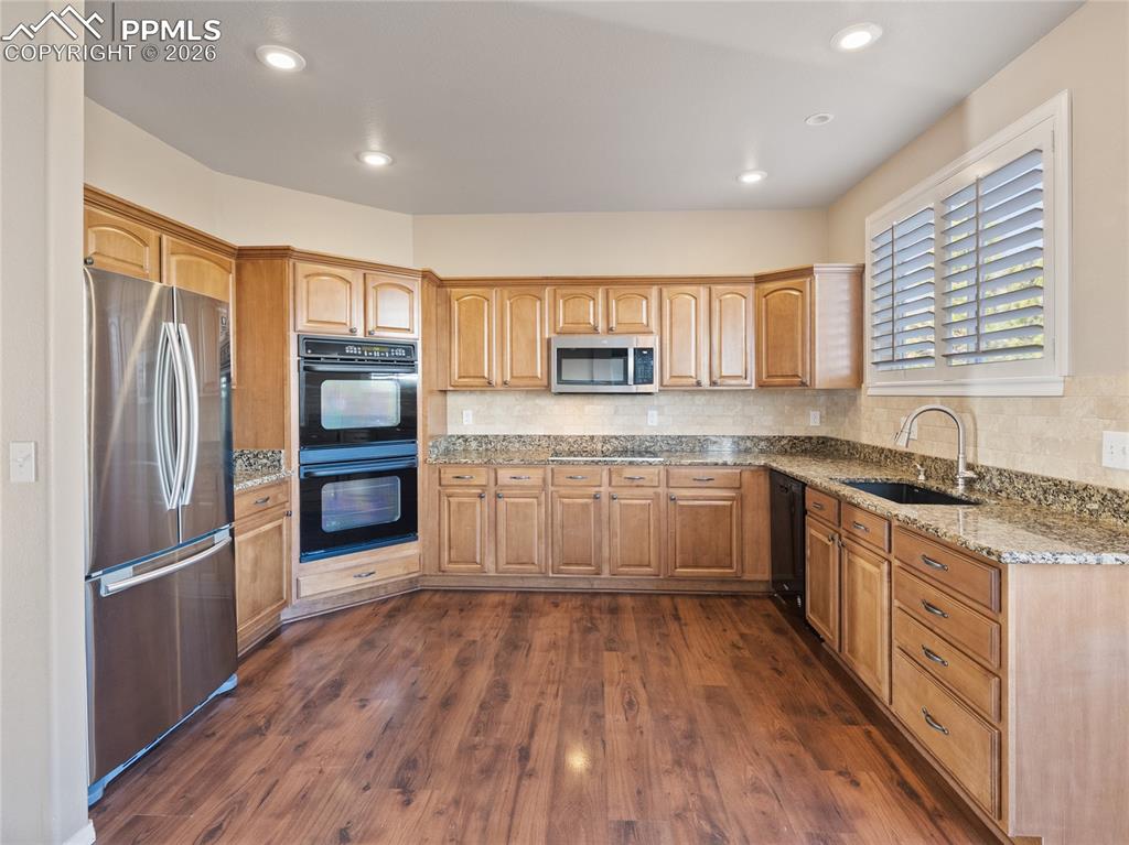Image 5 of 46: Kitchen featuring black appliances, light stone countertops, dark wood-type