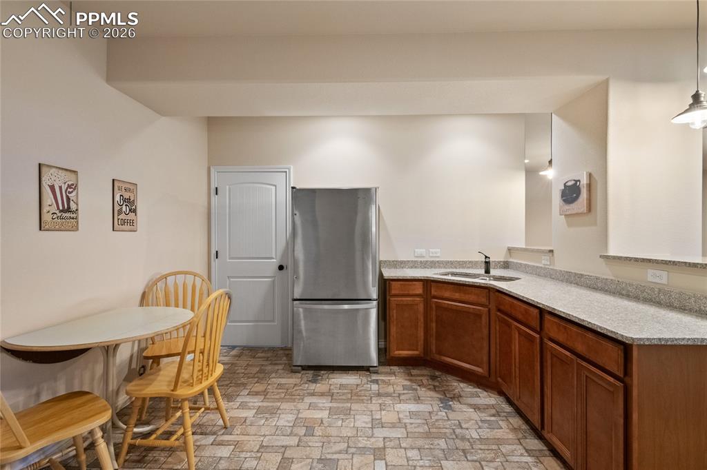 Image 37 of 49: Lower level wet bar with tile flooring, granite counter, full-sized fridge,