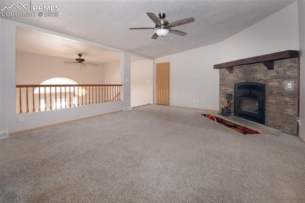 Image 10 of 50: Living room featuring carpet, vaulted ceiling, and a stone fireplace