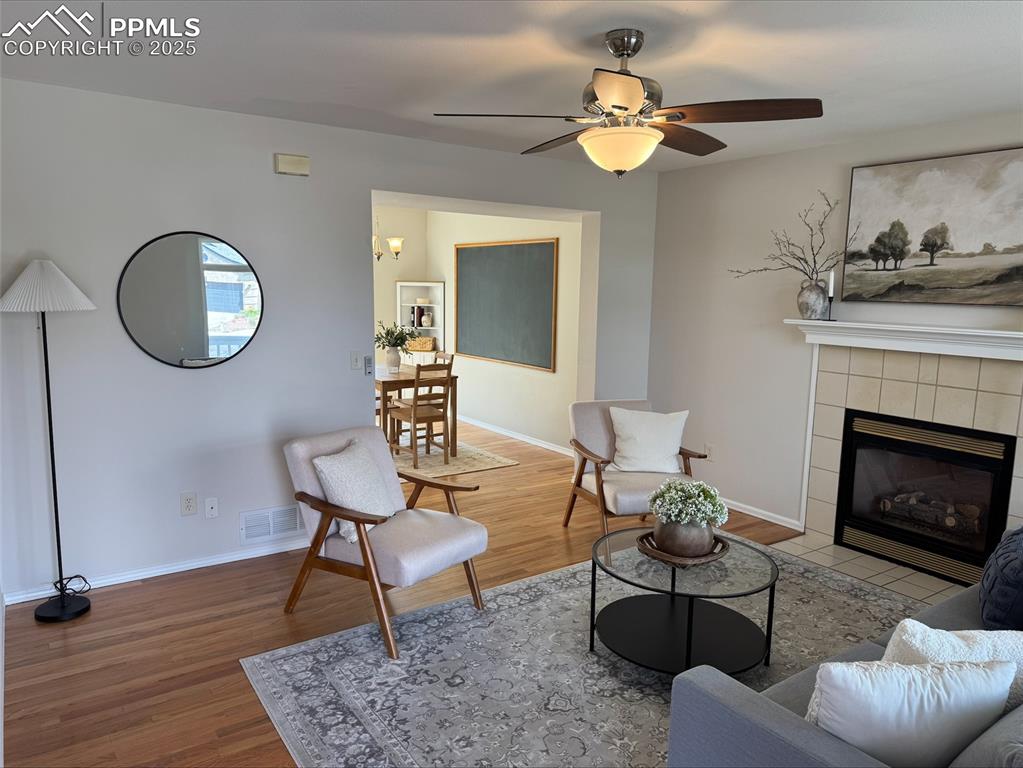 Image 12 of 45: Living room featuring oak floors, ceiling fan, and a fireplace