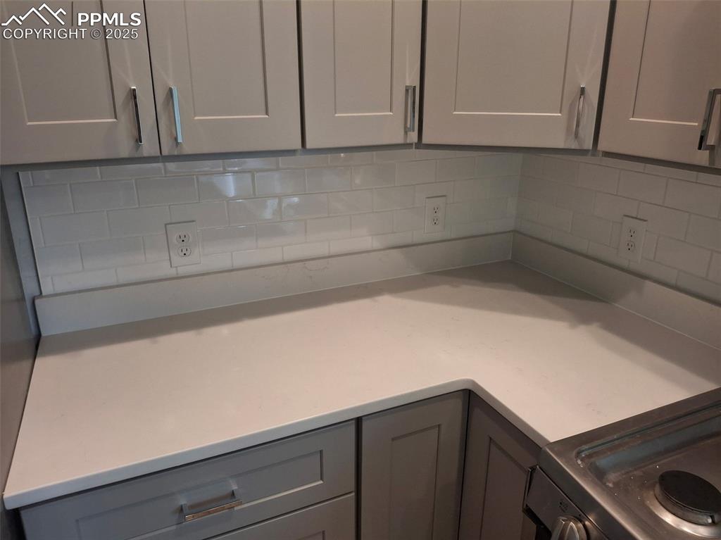 Image 7 of 45: Kitchen with gray cabinets, light countertops, and decorative tile backspla